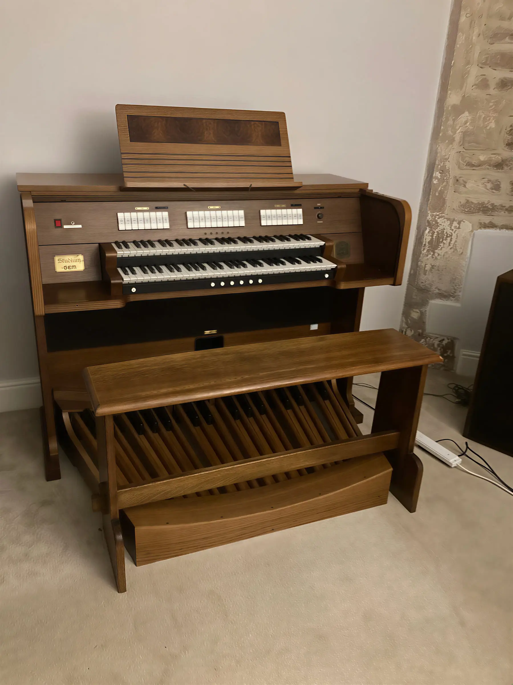 A wooden church organ with two keyboards and a pedalboard standing against a wall