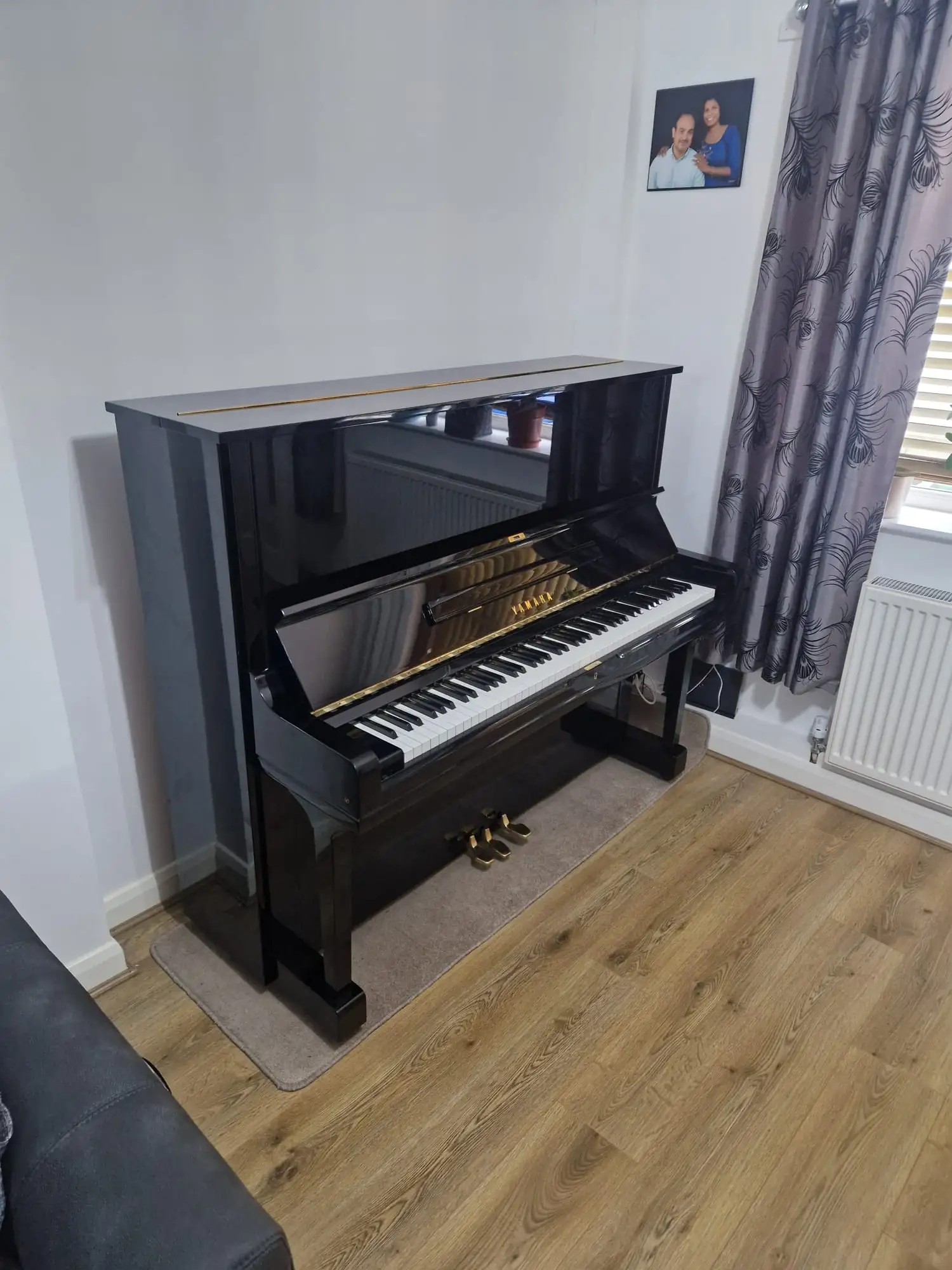 An upright piano wrapped in quilted blankets and strapped to a wall, with piano skates beside it