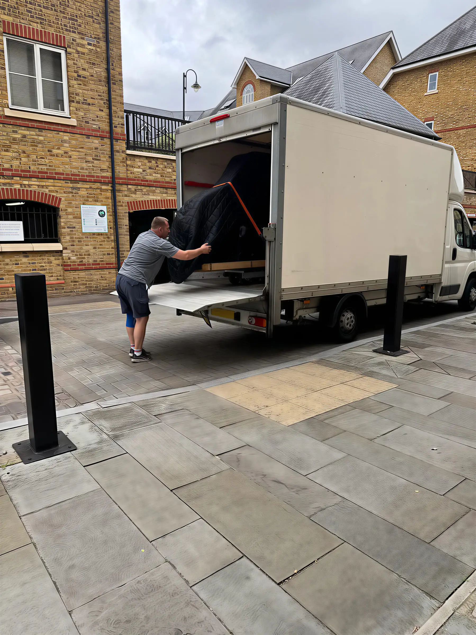 A mover pushing a wrapped piano up the tail lift into the back of the VVM van