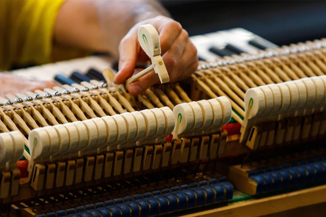 A tuner working on the pins inside an upright piano