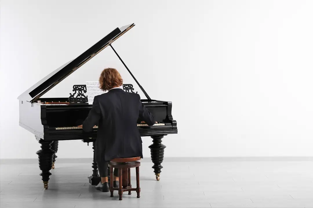 Somebody sitting down to play a grand piano in a bright room