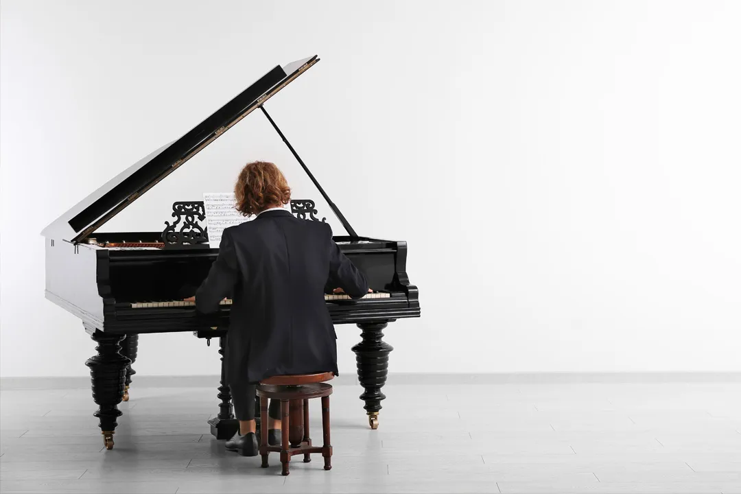 Somebody sitting down to play a grand piano in a bright room
